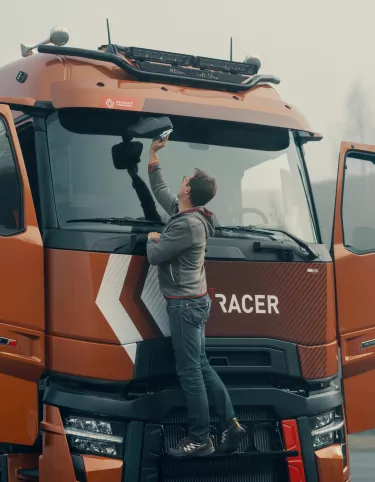 Model year 2025 : Renault Trucks T High Smart Racer : lifestyle (Renault Trucks Hero Zip Hoodie) driver on windshield access steps cleaning rearview mirror)
